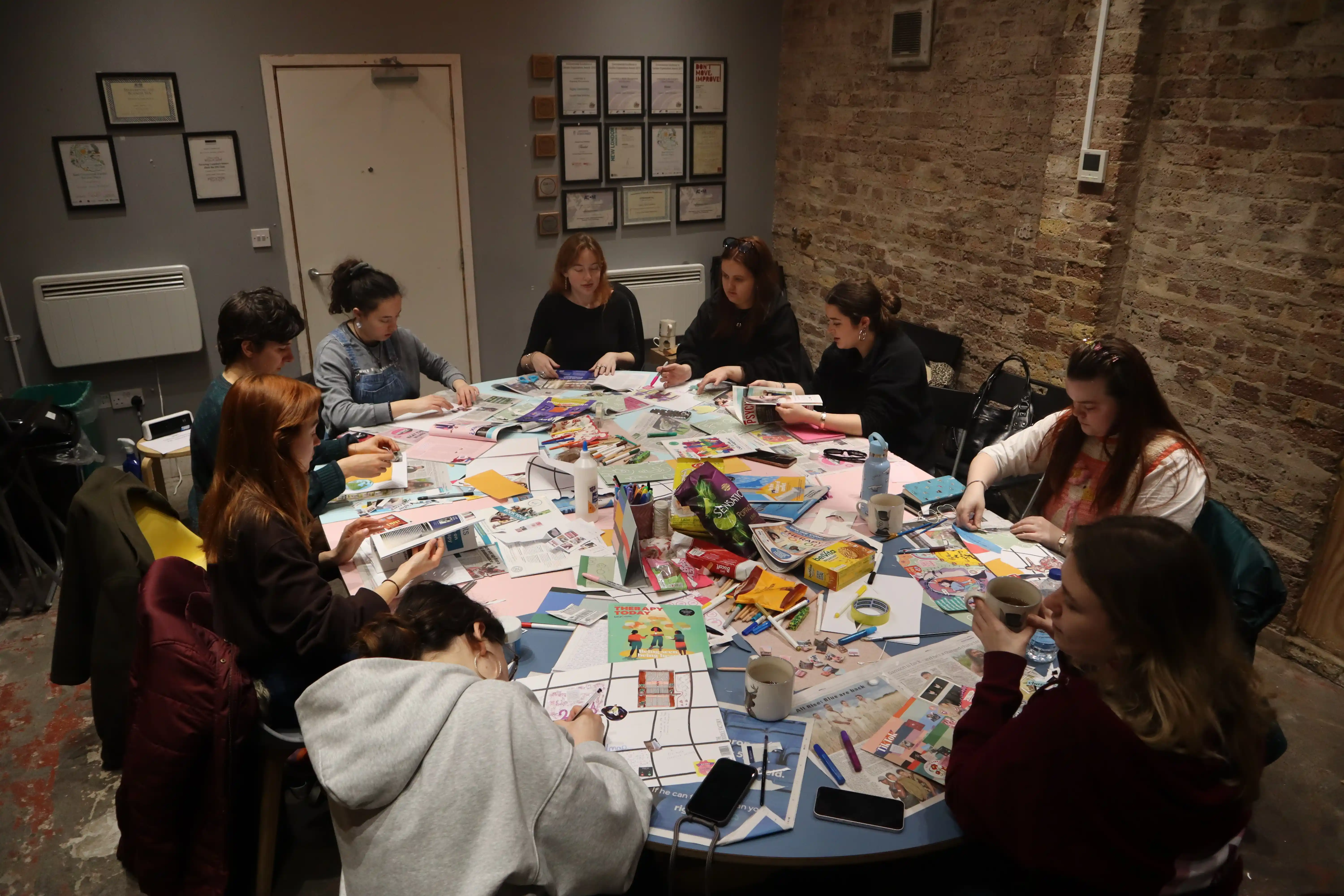 snapshot for a table covered in work, crafts, and snacks with 9 members collaborating