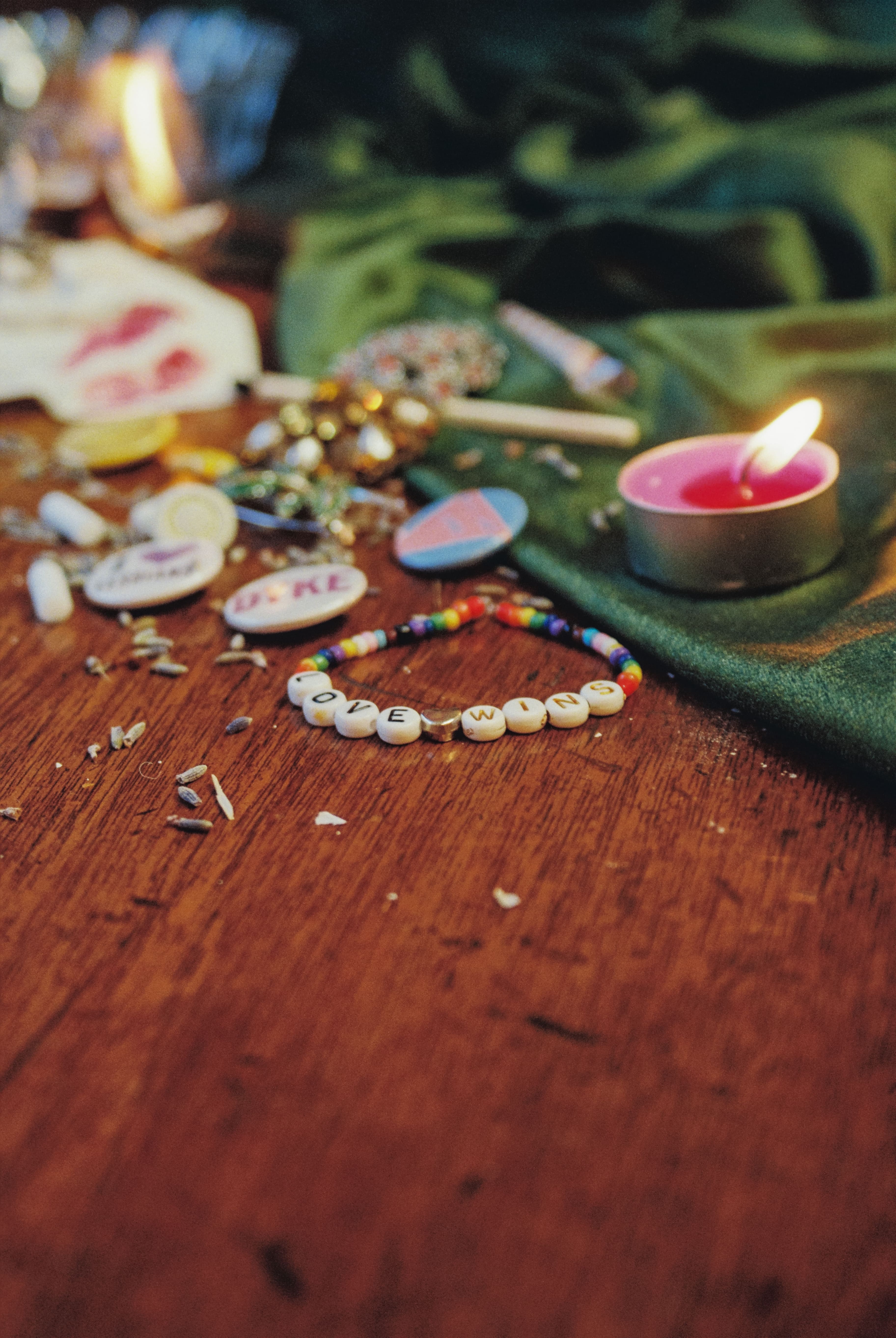 On a table lies artefacts from LGBTQ+ history. Including lesbian badges from the 1970s and pieces of discarded lavender sprigs. In the forefront is a modern day friendship bracelet with beads that spell out 'Love Wins'.