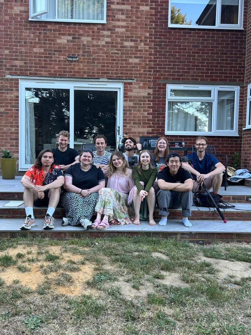 snapshot of cast and crew sitting on the steps outside a house