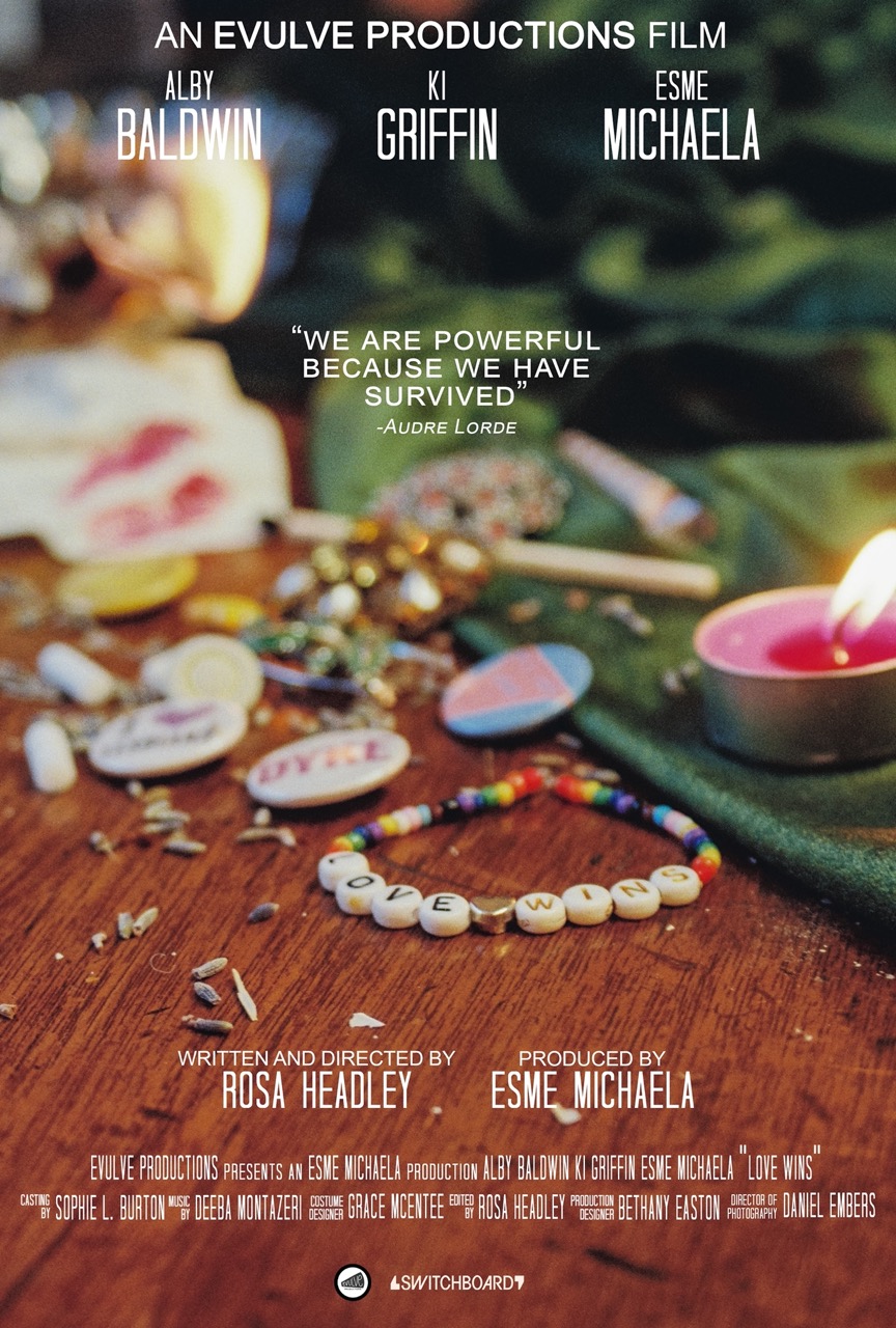 On a table lies artefacts from LGBTQ+ history. Including lesbian badges from the 1970s and pieces of discarded lavender sprigs. In the forefront is a modern day friendship bracelet with beads that spell out 'Love Wins'.